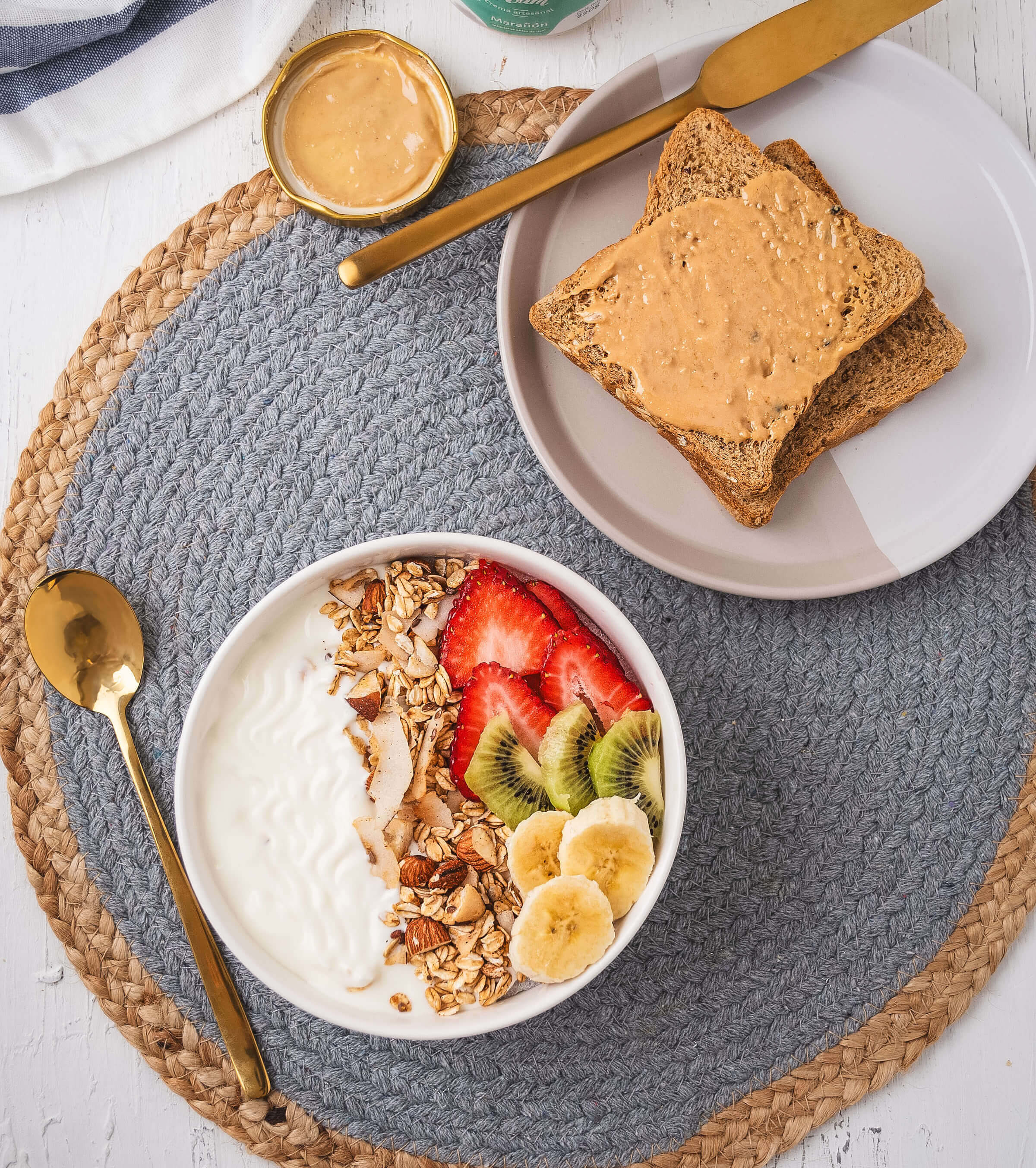 Frasco de Crema de marañón Kyniut artesanal de 220g, 100% natural, destacando su textura suave y cremosa junto a un bowl de yogurt, granola y frutas, y un par de tostadas untadas de crema.
